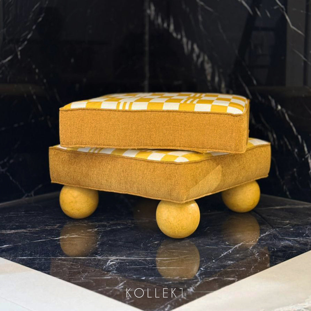 Yellow ottoman with checkered cushion on a dark marble surface, brand 'KOLLEKT' visible.